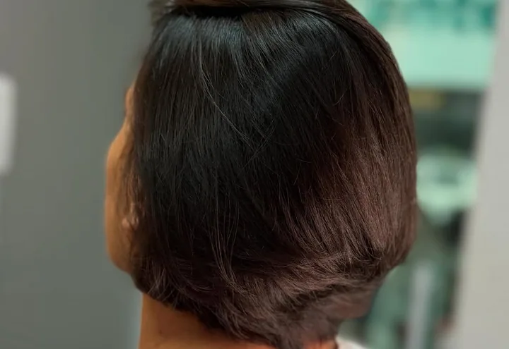 Corte curto escuro com acabamento arredondado na nuca, visto de lado