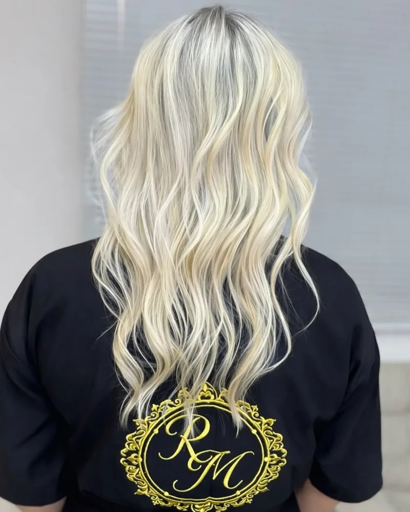 Cabelo loiro platinado em ondas, visto de costas, com o brasão RM bordado na peça do studio