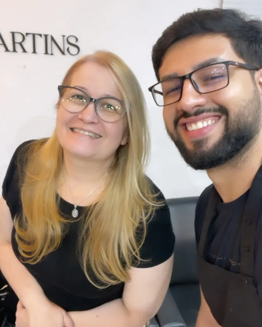Richard Martins sorrindo ao lado de uma cliente no studio, com o letreiro Richard Martins Studio na parede